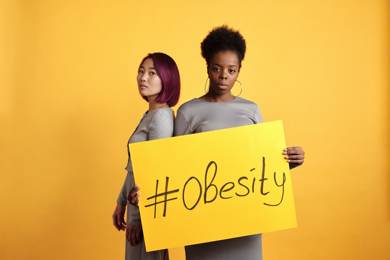 two women holding a placard that reads #obesity