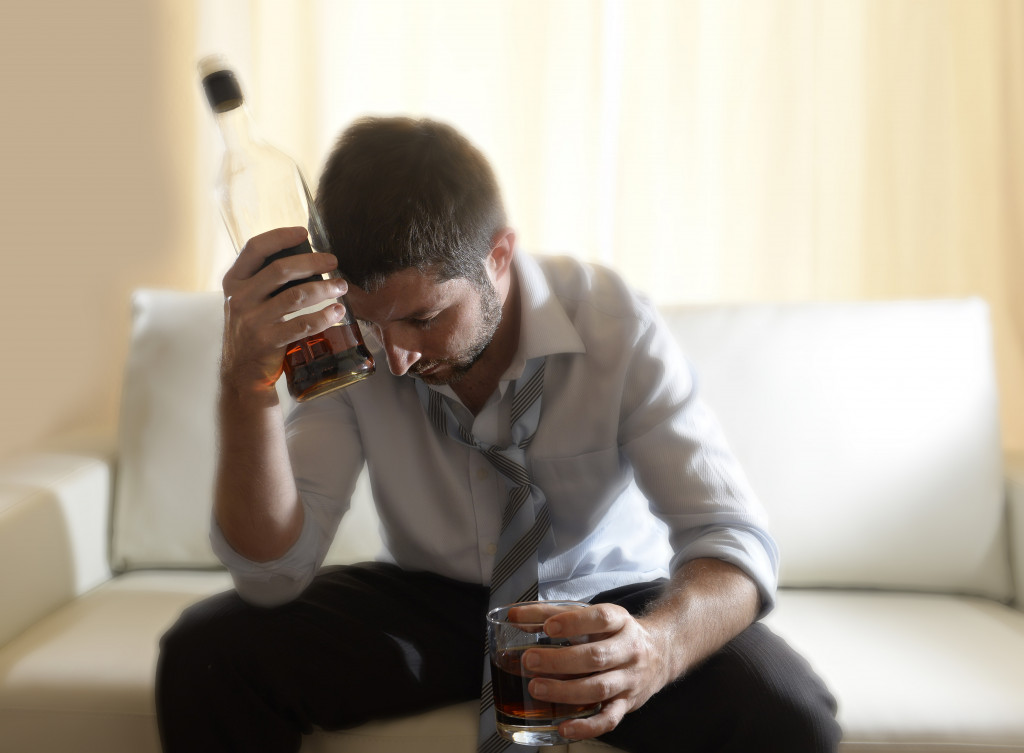 Man holds bottle and glass of alcohol while at home