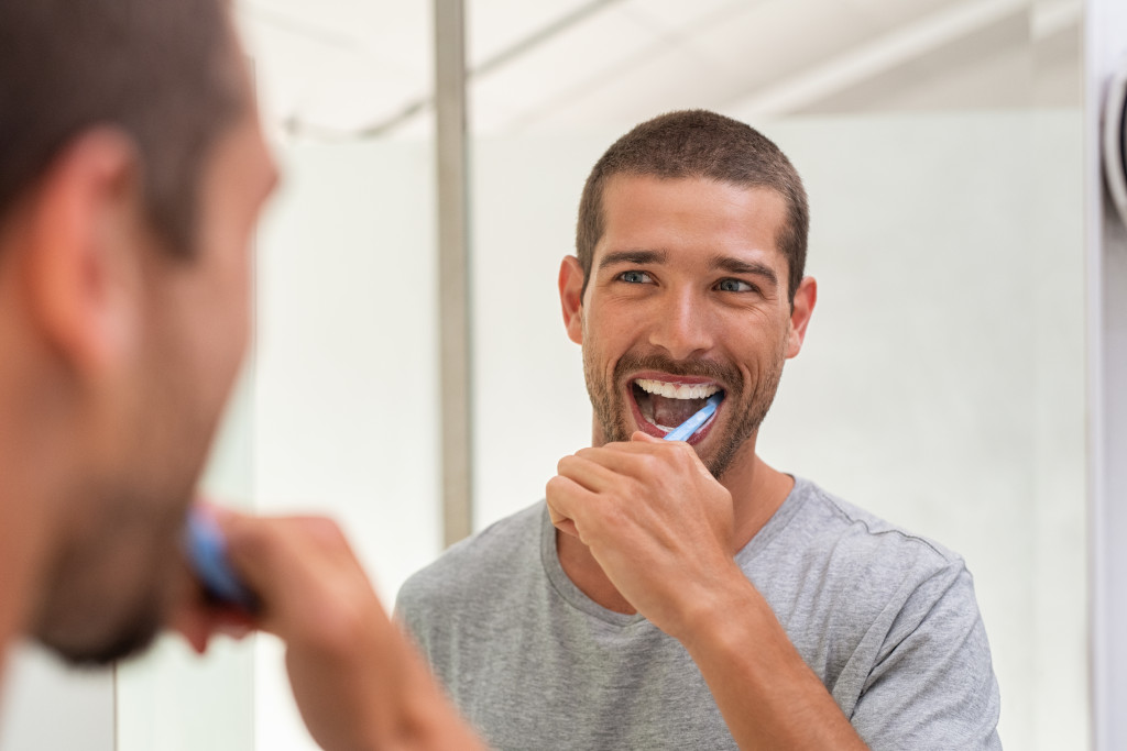 man brushing his teeth smiling in the mirror
